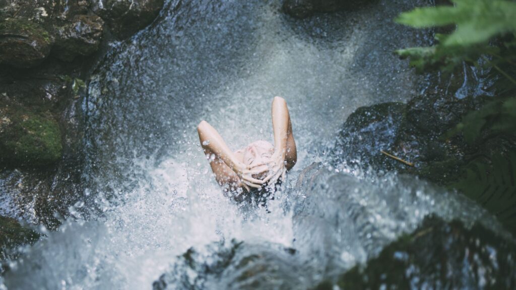 Frau duscht unter Wasserfall