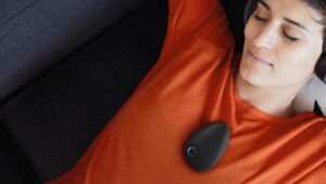 Frau liegt entspannt auf dem Sofa mit Sensate-Gerät auf dem Brustbein und Kopfhörern – Anwendung zur Beruhigung des Nervensystems