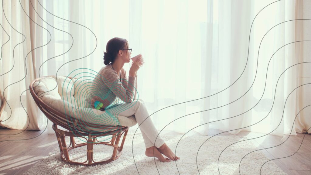 Frau sitzt entspannt in einem Sessel mit Kaffeetasse, umgeben von abstrahierten EMF-Linien; ein aktives Feld um ihren Körper visualisiert den Schutzmechanismus des Vivobase Move zur Stabilisierung der Zellkommunikation trotz elektromagnetischer Strahlung