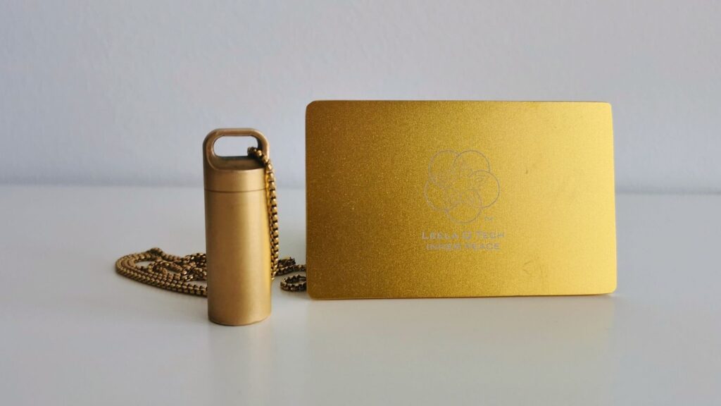 Leela Quantum Tech HEAL 360 Kapsel und goldene Frequenzkarte auf weißem Untergrund