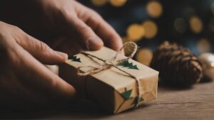 Nahaufnahme von Händen, die ein weihnachtlich verpacktes Geschenk mit Kordelband halten – minimalistischer Biohacking-Geschenkstil