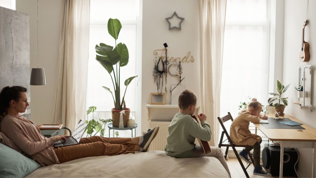 Frau liegt erschöpft auf Sofa mit zwei Kindern im Zimmer - mehr Verantwortung ab 30