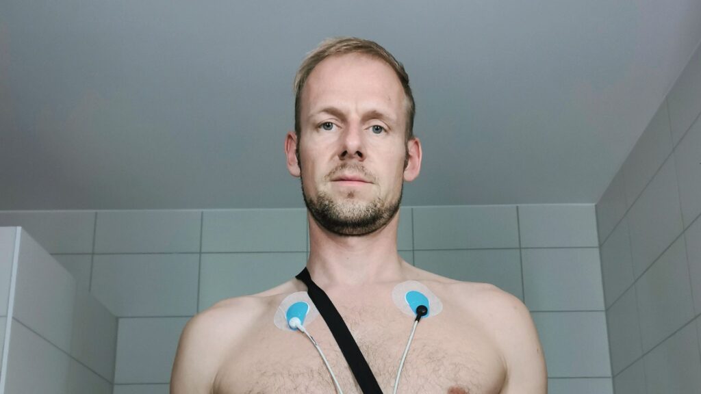 Mann trägt Langzeit-EKG zur Herzfrequenzmessung und blickt frontal in die Kamera.
